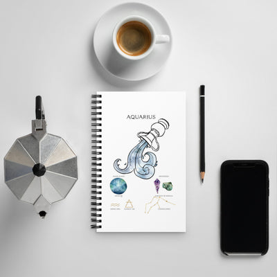Notebook with Aquarius design, coffee cup, phone, and other items on a light gray background