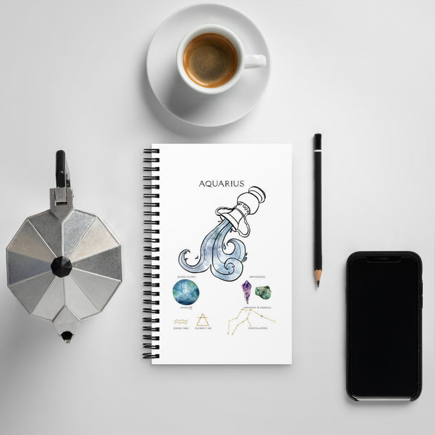 Notebook with Aquarius design, coffee cup, phone, and other items on a light gray background