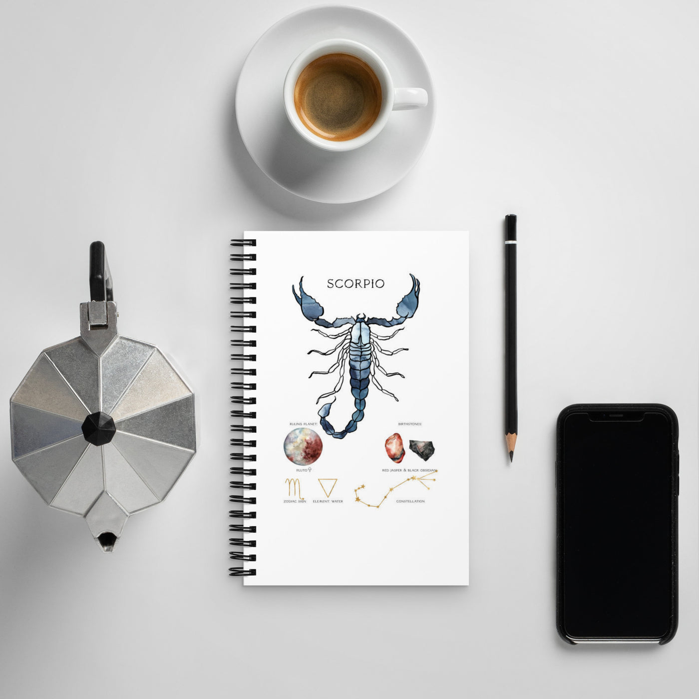 Notebook with Scorpio zodiac design, coffee cup, phone, and other items on a light gray surface