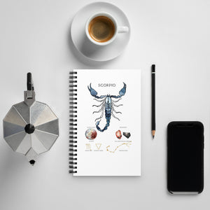 Notebook with Scorpio zodiac design, coffee cup, phone, and other items on a light gray surface