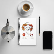 Notebook with Aries illustration, coffee cup, phone, and other items on a light gray surface