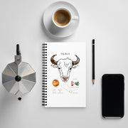 Notebook with Taurus illustration, coffee cup, phone, and other items on a light gray background