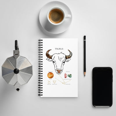 Notebook with Taurus illustration, coffee cup, phone, and other items on a light gray background