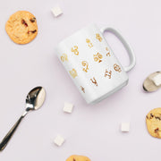White mug with gold symbols, cookies, and a spoon on a light purple background