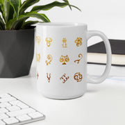 White mug with gold astrological symbol designs on a desk with a plant and books in the background
